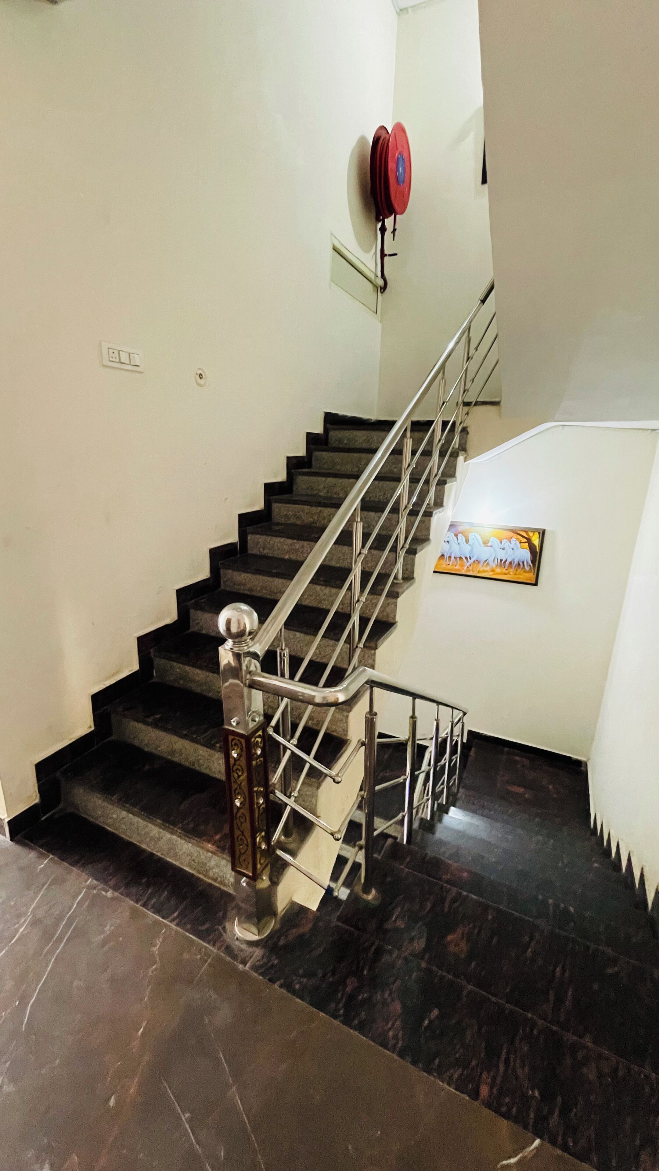 A staircase with metal railings, a wall-mounted red object, and a framed picture of horses.