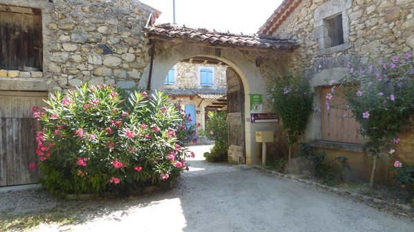 A stone archway leading to a building with a blue door and a sign reading "Le Mas' Michel".