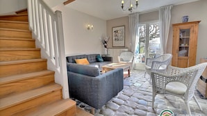 A living room with a sofa, a chair, a table, a staircase, and a view through a glass door. - Spacious, bright gîte, ideal for large families or groups of friends. (Ruoms)