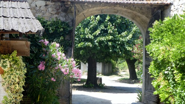 A stone archway leading to a garden with a pergola and flowering plants. - Spacious, bright gîte, ideal for large families or groups of friends. (Ruoms)