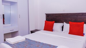 Una cama bien hecha con ropa de cama blanca y almohadas rojas, un cabecero de madera y un armario blanco con espejo.