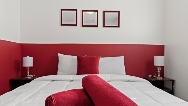 A neatly made bed with white and red bedding, two bedside tables with lamps, and three framed mirrors on the wall.