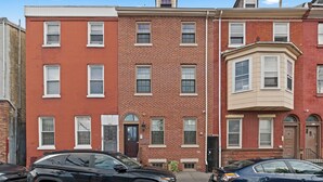 A row of red brick townhouses with white-framed windows, a central door, and a bay window on the right.