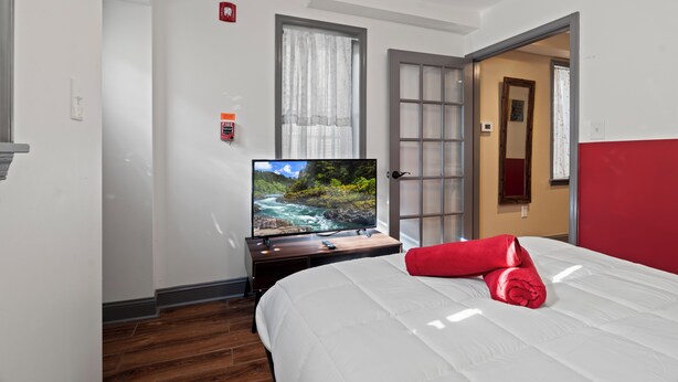 Habitación de hotel con cama, televisor mostrando una escena natural, toalla roja y puerta que da a otra habitación.