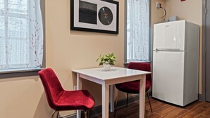 A small kitchenette with a white refrigerator, a framed AC/DC album, and a potted plant on the counter.