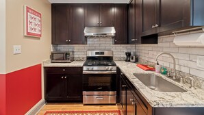 A kitchen with dark wooden cabinets, stainless steel appliances, a granite countertop, and a tiled backsplash.