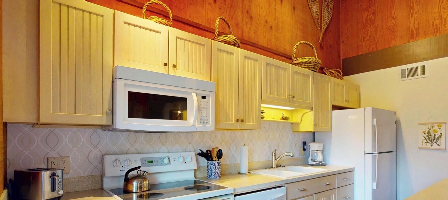 A kitchen with white cabinetry, a microwave, stove, and dishwasher. There are baskets on the upper cabinets and a coffee maker on the counter.