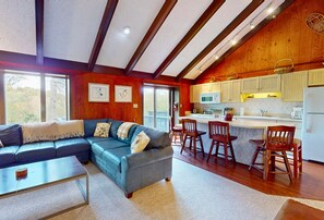 A cozy living room with a sectional sofa, a coffee table, and a kitchen area with wooden cabinets and a bar.