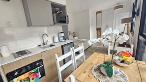 A modern kitchen with a built-in oven, microwave, and coffee maker. There is a dining table with chairs and a decorative plant.