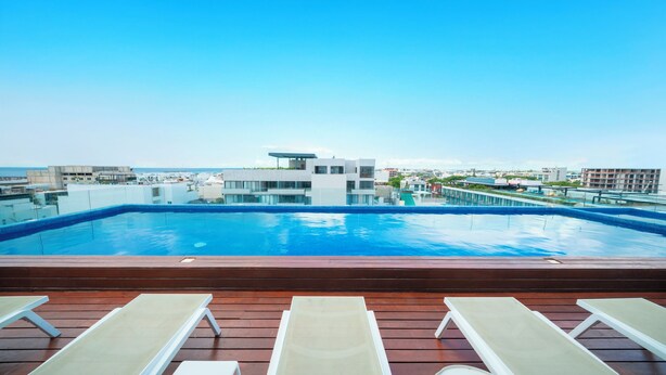 A rooftop swimming pool with lounge chairs, a clear view of the cityscape, and a modern building in the background. - 1 Bedroom Pool & Gym - Piedra Azul 605 (Playa del Carmen)