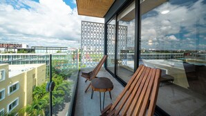 A balcony with wooden furniture, a glass partition, and a view of the cityscape. - 1 Bedroom Pool & Gym - Piedra Azul 605 (Playa del Carmen)