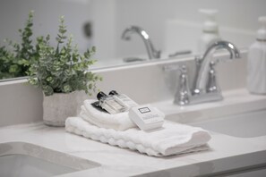 A bathroom with a white sink, a mirror, a potted plant, and toiletries.