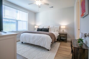 A bedroom with a bed, bedside tables, a desk, a ceiling fan, and a window with blinds.