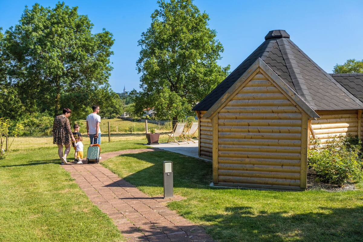 A wooden cabin with a sloped roof, surrounded by a grassy area and trees.