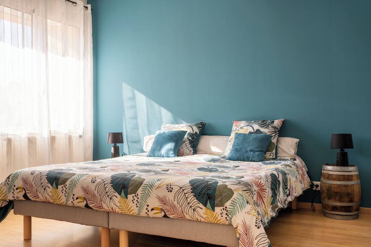 A bedroom with a bed, pillows, a lamp, and a wooden barrel.