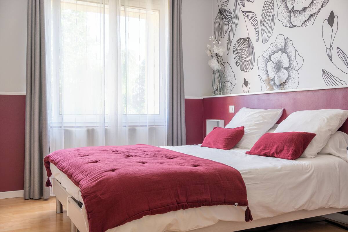 A bedroom with a bed, curtains, and a floral wall design.