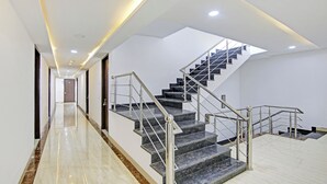 Interior moderno de un hotel, con un largo pasillo, una escalera con barandillas metálicas y un tragaluz sobre la escalera.