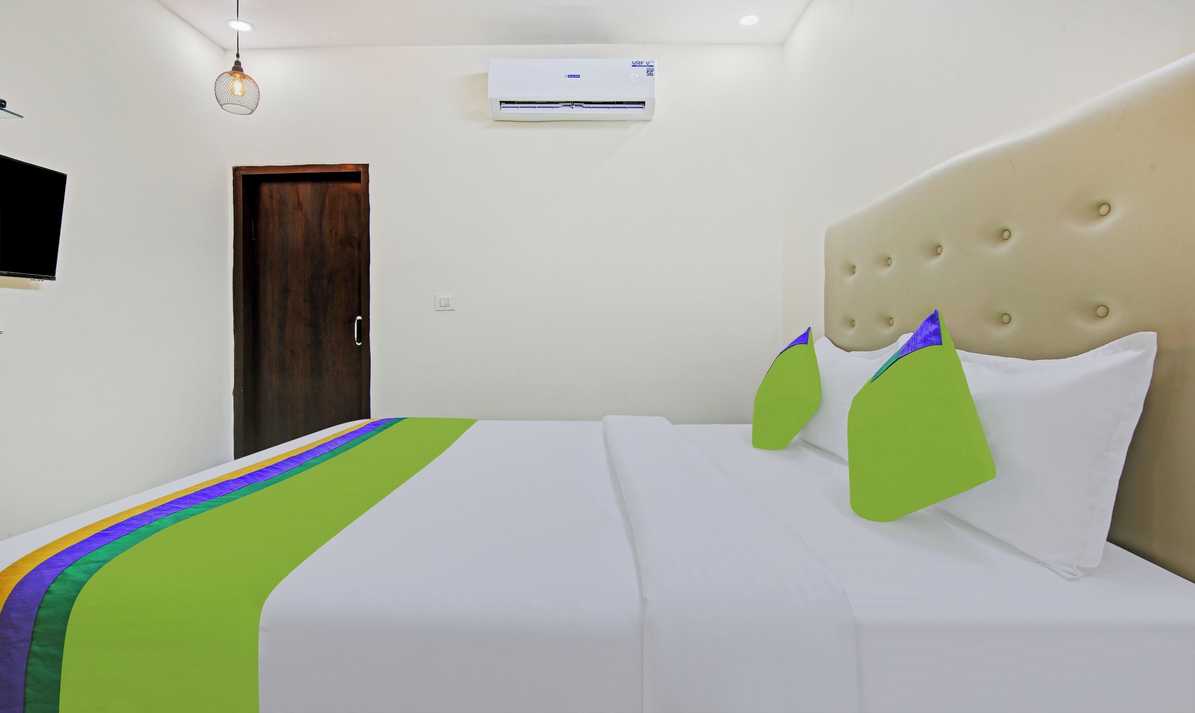 A hotel room with a bed, a door, an air conditioning unit, and a wall-mounted television.