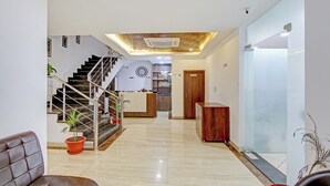Un moderno vestíbulo de hotel con piso de mármol, una escalera, mostrador de recepción y un muro divisor de vidrio.