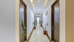 Un pasillo de hotel con piso de mármol, plantas en macetas y puertas de madera.