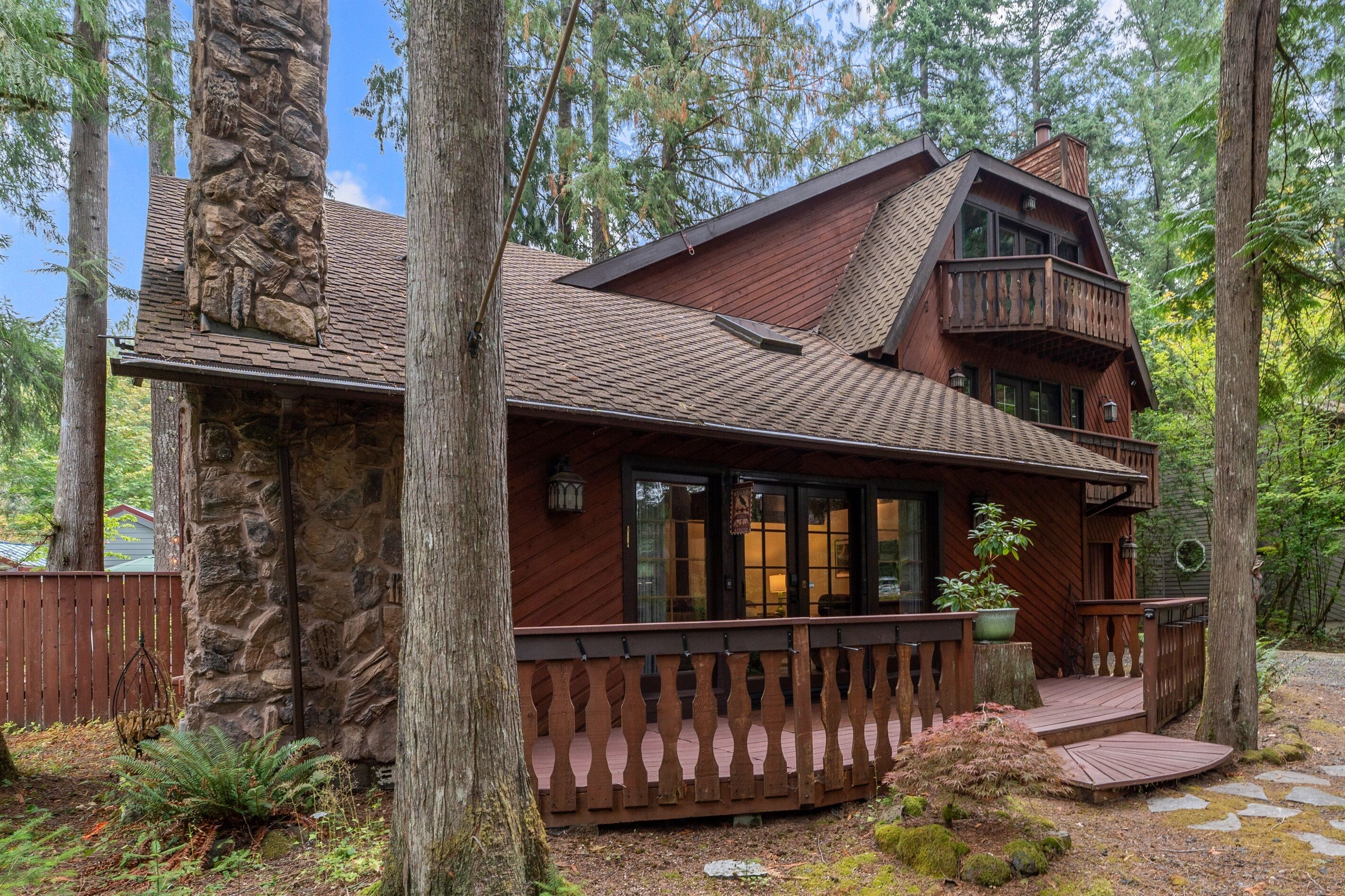 A rustic cabin with a stone chimney, wooden deck, and large windows.