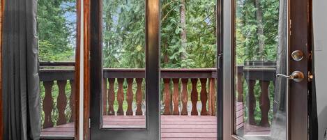 Une terrasse en bois avec une porte vitrée donnant sur une zone boisée.