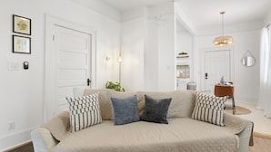 Una sala de estar moderna con un sofá color beige, dos almohadones estampados, una lámpara de pie y un colgador de techo.