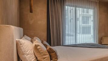 Une chambre à coucher avec un lit, des oreillers, un ventilateur de plafond et une fenêtre avec des rideaux légers.