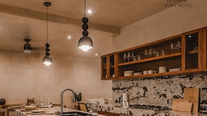 A kitchen with a marble island, wooden bar stools, and a wooden upper shelf with glassware. - JUNAB HOUSE - HOUSE (The Cuyo)