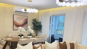 A modern living room with a beige sectional sofa, a dining table with chairs, a potted plant, and a large window with curtains.