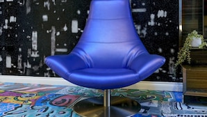 Una silla azul con base metálica en una habitación con pared abstracta blanco y negro y grafitis coloridos en el suelo.