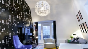 Un salón moderno con una pared de diseño blanco y negro, una silla blanca redonda, una silla azul, una mesa blanca y una alfombra amarilla.