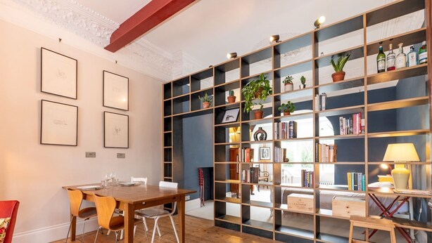 Une pièce comprenant une table à manger en bois, des chaises, une bibliothèque et un lit avec une tête de lit rouge.