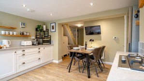 A modern kitchen with white cabinetry, a dining area with a wooden table and chairs, and a staircase leading to another level. - Pass the Keys | Charming 2 Bed Townhouse Short Walk To The River (Shrewsbury)