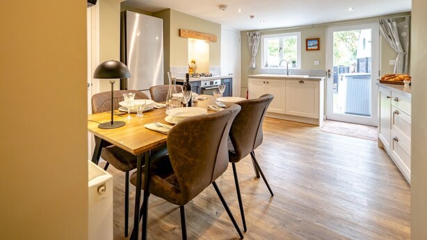 A modern kitchen with white cabinets, a dining area with a wooden table and chairs, and a view of the backyard through a glass door. - Pass the Keys | Charming 2 Bed Townhouse Short Walk To The River (Shrewsbury)