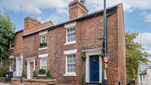 A two-story brick house with a blue front door, white window frames, and a small front garden. - Pass the Keys | Charming 2 Bed Townhouse Short Walk To The River (Shrewsbury)