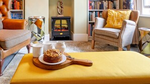 A cozy living room with a fireplace, bookshelves, a comfortable armchair, and a table with a cake. - Pass the Keys | Charming 2 Bed Townhouse Short Walk To The River (Shrewsbury)