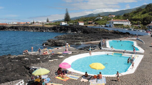 A beach with a swimming pool surrounded by people.