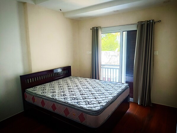 A single bed with a patterned mattress in a room with plain walls and a window with curtains.
