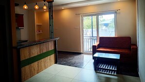 Un interior moderno con área de cocina, zona de estar con sofá y mesa de centro, y puerta corrediza de vidrio que da a un balcón exterior.