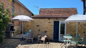 A stone building with a tiled roof, outdoor seating area with chairs and tables, and a wooden deck. - Gîte Les Lauzes "A precious interlude in the heart of the Périgord Noir". (Saint-Avit-de-Vialard)
