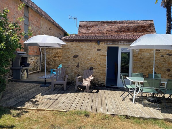 A stone building with a tiled roof, outdoor seating area with chairs and tables, and a wooden deck. - Gîte Les Lauzes "A precious interlude in the heart of the Périgord Noir". (Saint-Avit-de-Vialard)