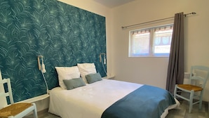 A bedroom with a bed, two chairs, a window with curtains, and a wall with a leaf pattern. - Gîte Les Lauzes "A precious interlude in the heart of the Périgord Noir". (Saint-Avit-de-Vialard)