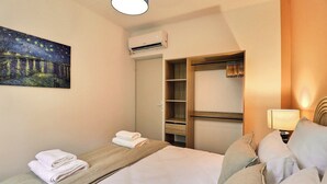 A hotel room with a bed, a painting of a night scene, an air conditioning unit, a wardrobe, and a bedside lamp. - Nuit Étoilée - Cocoon in the Heart of Arles - A/C (Arles)