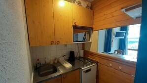A compact kitchen with wooden cabinets, a built-in microwave, and a window with curtains.