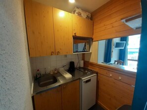 A compact kitchen with wooden cabinets, a built-in microwave, and a window with curtains. - 100 meters to the shops, 2nd floor, view of the station/ski lifts, TV, locker for skis (Valfréjus)