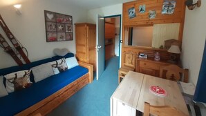 A compact room with a blue sofa, wooden cabinets, a small table, and a mirror.