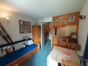 A compact room with a blue sofa, wooden cabinets, a small table, and a mirror. - 100 meters to the shops, 2nd floor, view of the station/ski lifts, TV, locker for skis (Valfréjus)