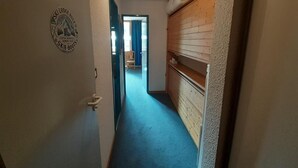 A narrow hallway with a blue carpet, a wooden cabinet on the right, and a door with a ski lodge sign on the left.