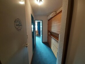 A narrow hallway with a blue carpet, a wooden cabinet on the right, and a door with a ski lodge sign on the left. - 100 meters to the shops, 2nd floor, view of the station/ski lifts, TV, locker for skis (Valfréjus)